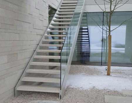 Stahltreppe mit Natursteinstufen und Nurglasgeländer