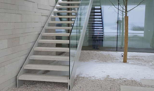 Stahltreppe mit Natursteinstufen und Nurglasgeländer